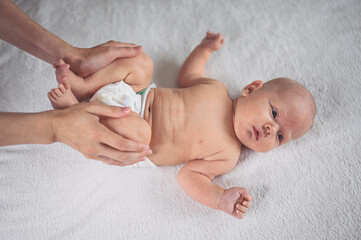 Mother is changing diaper for cute emotional funny newborn little infant baby boy laying in crib