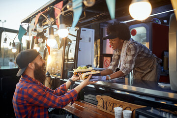 caucasian beardy hipster taking two sandwiches from polite female afro-american employee in fast food service