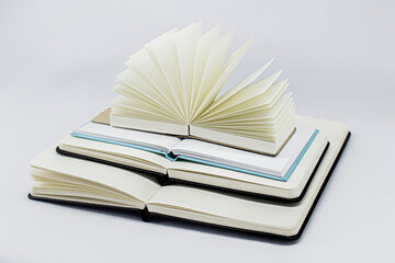 Unfold notebooks lie on top of each other. Fan open notepad with blank light beige pages on the top of pyramid of books. White backdrop.