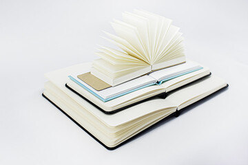 Four unfold notebooks lie on top of each other. Fan open notepad with blank light beige pages. White background