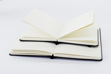 Two unfold black notebooks lie on top of each other. Open notepads with blank light beige pages. White background
