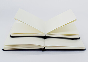Black open small notepad and unfold large notebook with blank light beige pages. White background