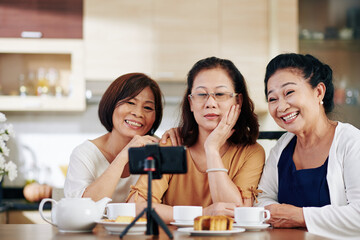Group of happy elderly women talking selfie on smartphone when sitting at kitchen table