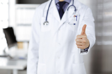 Unknown male doctor standing with thumbs up sign in clinic near his working place, closeup. Perfect medical service in hospital. Medicine and healthcare concept