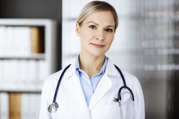 Friendly female doctor standing in clinic. Portrait of cheerful smiling physician. Perfect medical service in hospital. Medicine and healthcare concept