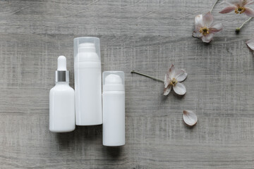 Fototapeta na wymiar white bottles for cream and serum on a gray table with fresh flowers