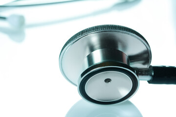 Stethoscope head on glossy white table, the black phonendoscope, close up on white background,