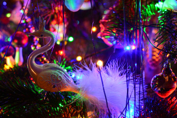 Fototapeta na wymiar Christmas tree holiday background with glass swan, balls, and lights. Colorful decoration close-up in low-key lighting.