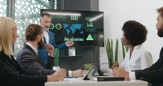 Briefing in company where confident experienced successful bearded expert using interactive whiteboard to show his multiethnic attantive listeners problematic ecological zones on our earth