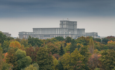 Fototapeta na wymiar Palace of the Parliament building in Bucharest - top view with a cloudy sky above and autumn fall trees in foreground