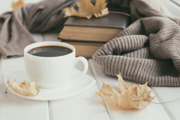 Warm wool sweater, cup of coffee, old books with autumn leaves on white wooden boards. Cozy home reading, hygge concept