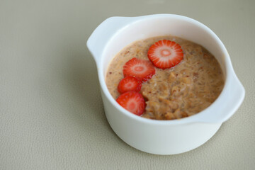 Buckwheat sereal with strawberry slices in white bowl on grey background, copy space