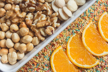 An assortment of mixed dry fruit, walnuts, almonds, and hazelnuts with orange slices on colored sugar noodles. Creative cooking desserts. Fruits and candies.
