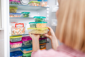 Woman putting containers with frozen mixed vegetables from refrigerator.