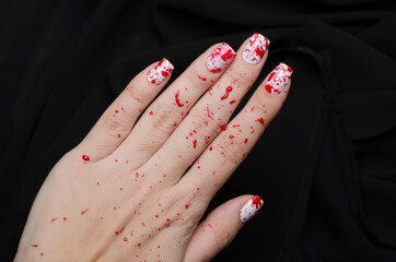 Bloody manicure for Halloween with drops of blood and a fingerprint with a knife on a black...