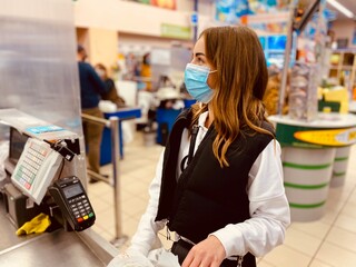 young beautiful girl in medical mask against coronavirus at checkout in supermarket