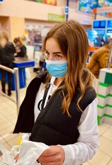 young beautiful girl in medical mask against coronavirus at checkout in supermarket