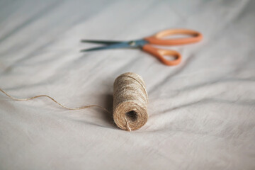 On the soft light fabric lies a coil of coarse hemp rope and modern sharp scissors. Sewing and...