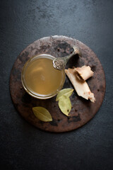 A glass jar of fresh beef bone broth with spices on an aged round stand and a vintage spoon on the side. The concept of a healthy diet rich in vitamins, collagen and amino acids. Flat lay,low key.