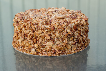 Beatiful nut biscuit cake finished with crushed sugar-coated candied caramelized almonds on a glass table