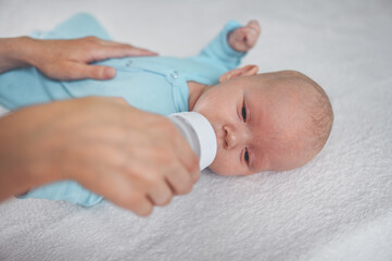 Cute emotional funny newborn infant boy laying on bed with milk bottle. Baby facial expressions.