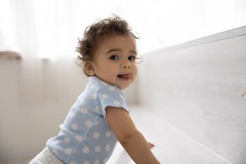 Portrait of cute small African American baby toddler child have fun on comfortable bed at home....