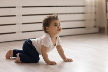 Cute small african American toddler baby child crawl on warm wooden home floor. Smiling little...