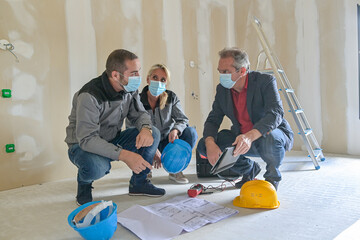 Professional meeting on a construction site between the architect and the craftsmen who wear a protective mask against covid-19