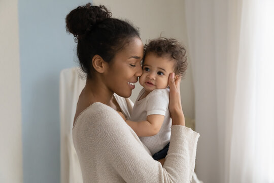 Happy young African American mom hold in hands hug cute little ethnic baby toddler show love care. Smiling biracial mother embrace cuddle small newborn infant child. Motherhood, childcare concept.