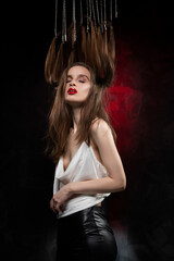 Fototapeta premium A beautiful girl with evening make-up and red lips wearing a blouse with a deep neckline and her hair suspended on chains, posing on a red and black background. Conceptual, avant-garde design