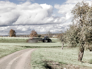 Fototapeta na wymiar tractor throwing cow manure on a meadow in autumn in Germany