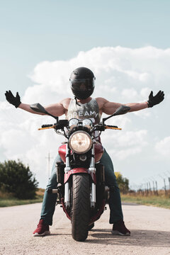 Male motorbike rider sitting on a red bike with wide open arms and wearing a safety helmet