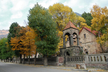 View on Medieval Orthodox Church in a village with autumn trees on a background of mountains in cloudy weather. Caucasus Mountains, Georgia.