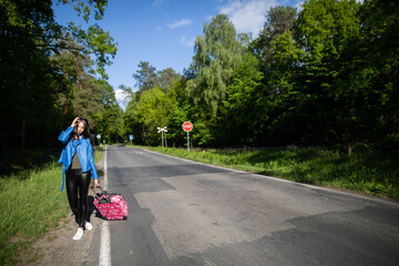 Fototapeta premium The teenager returns on foot along the asphalt road among lush greenery - wonderful trees and shrubs.