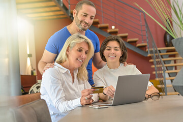Couple and their daughter in front of their laptop in their living room to buy her a gift on the internet with their credit card