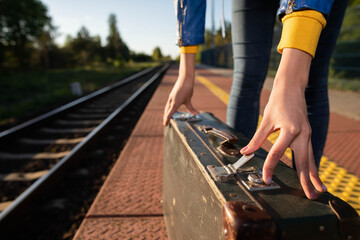 A girl fastens the zipper on an old travel suitcase on a train platform one summer afternoon during a planned train trip.