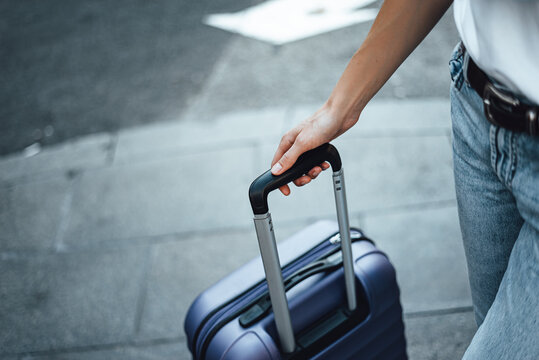Close-up of a female hand holding suitcase. Young traveling woman with luggage on a city street. Traveler on vacation.
