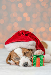 Jack russell terrier wearing eyeglasses and santa's hat sleeps and holds gift box on festive background. Empty space for text