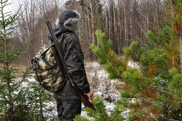 Hunter with a gun and a backpack in the winter forest