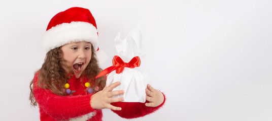 Emotional portrait of a little girl in a Santa hat with a gift in her hands, on a white background. The concept of a happy childhood. Big seasonal sale. Happy New year and merry Christmas