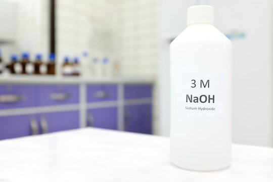 Selective focus of a plastic bottle of sodium hydroxide solution or NaOH chemical reagent. Chemistry research laboratory background with copy space.