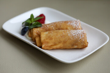 Rolled up stuffed thin pancakes with sourcream, mint leaf and raspberry on white background