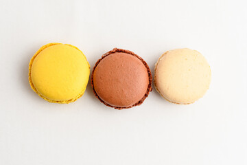 Top view of three sweet French macarons isolated on white background, flavours of lemon, vanilla and chocolate, pastel colors.