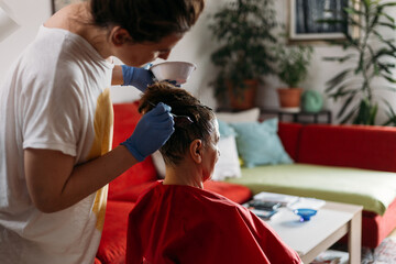 Middle-age woman helping her elderly mom in hair dyeing at home during Coronavirus pandemic