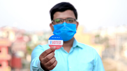Man from minority group holds I Voted sticker upclose to the camera rackfocus.