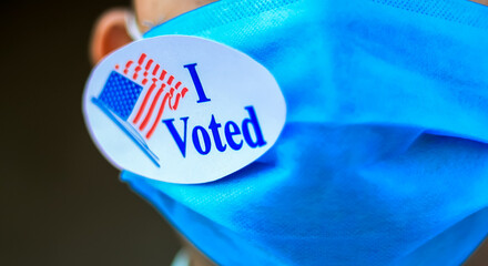 Voting during Coronavirus Pandemic concept. Man puts I Voted sticker with American Flag on the face mask.