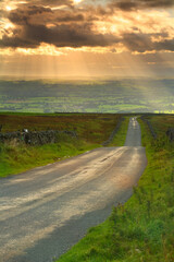 Country Road going into the distance with Crepuscular rays in the sky, Pennines, Cumbria, England,  United Kingdom
