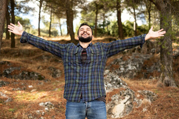 Man with beard and plaid shirt of aesthetic lumberjack spreads his arms in the middle of nature with joy