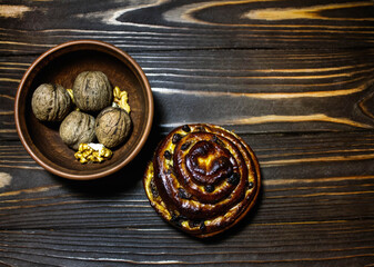 Fragrant bun with raisins and nuts in a clay bowl on a wooden background