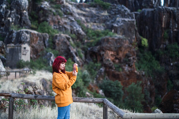 Chica peliroja en parque natural tomando fotogarfías 